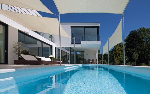 Moderner Pool mit schattenspendenden Sonnensegeln vor einer zeitgenössischen Villa.