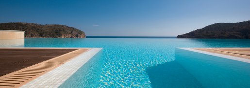 Infinity-Pool mit Blick auf das offene Meer und umliegende Hügel unter klarem Himmel.