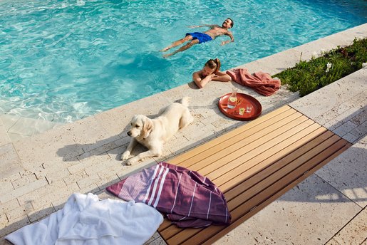 Entspannter Poolmoment mit schwimmendem Mann, Frau am Beckenrand und Hund im Vordergrund.