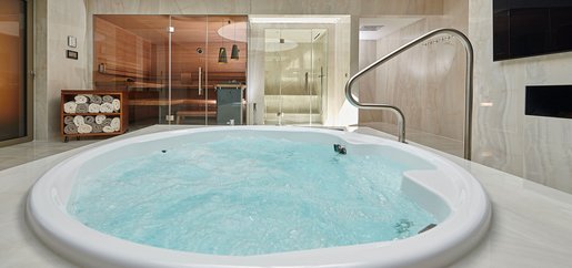 Exklusiver Spa-Bereich mit sprudelndem Whirlpool im Vordergrund, stilvoller Sauna mit Glasfront und modernem Dampfbad im Hintergrund.